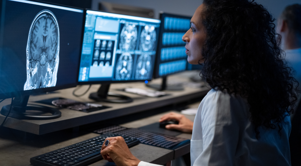 Photo of woman in lab coat at screens showing medical imaging